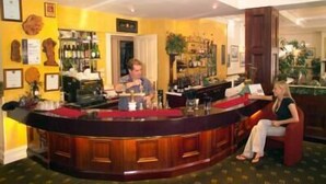 A bar area with a wooden counter, a bartender, and a seated guest. - Lucas Hotel (Latrobe)