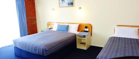 A hotel room with two beds, a brick wall, a window with blue curtains, and a painting on the wall.