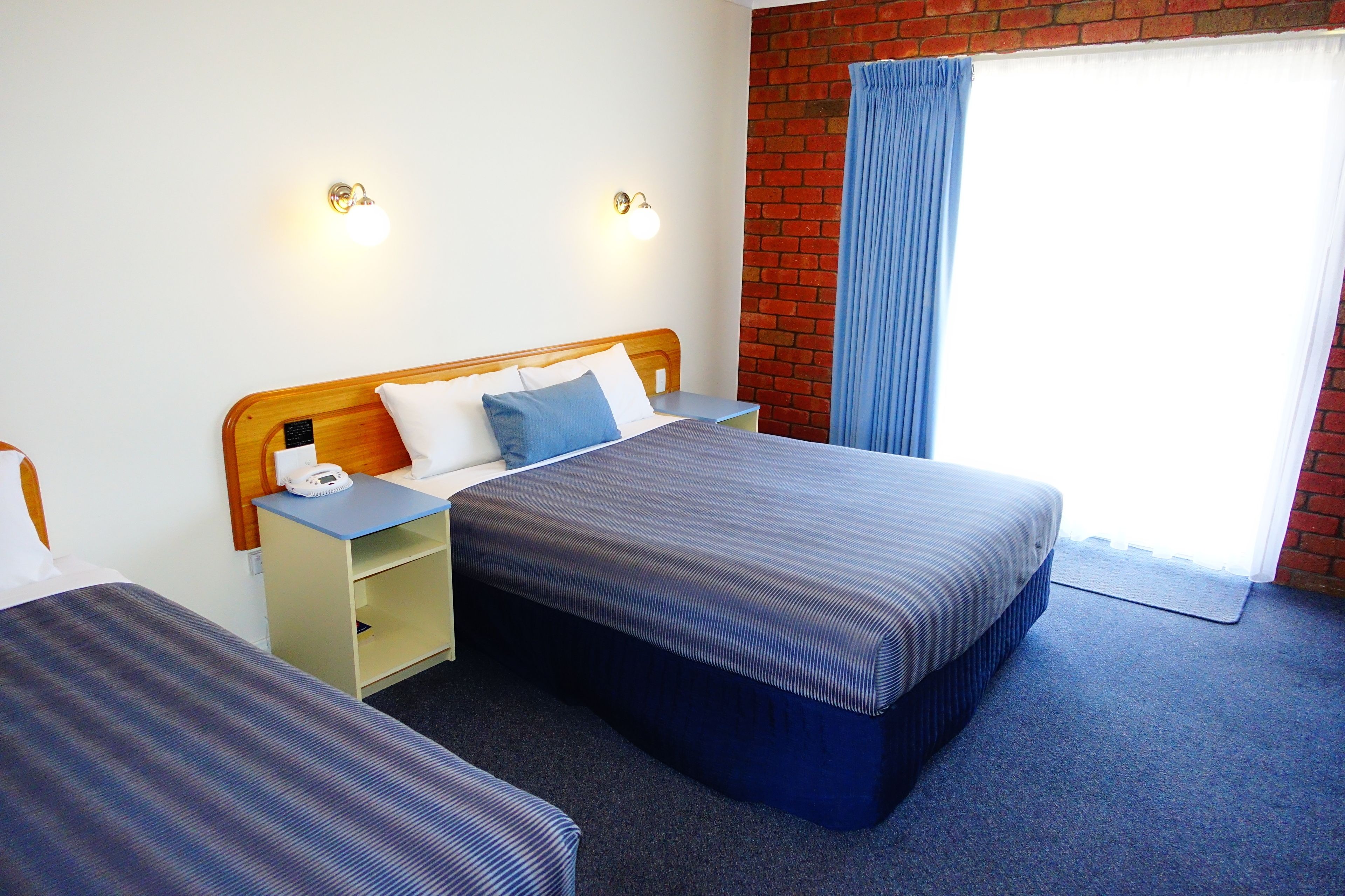 A hotel room with a bed, bedside tables, and a brick wall.