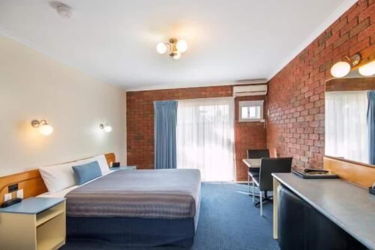 A hotel room with a bed, desk, chair, and a mirror.