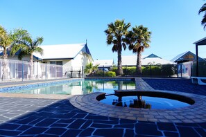 A swimming pool with a fountain, surrounded by palm trees and a white fence. - Torquay Tropicana Motel (Torquay)