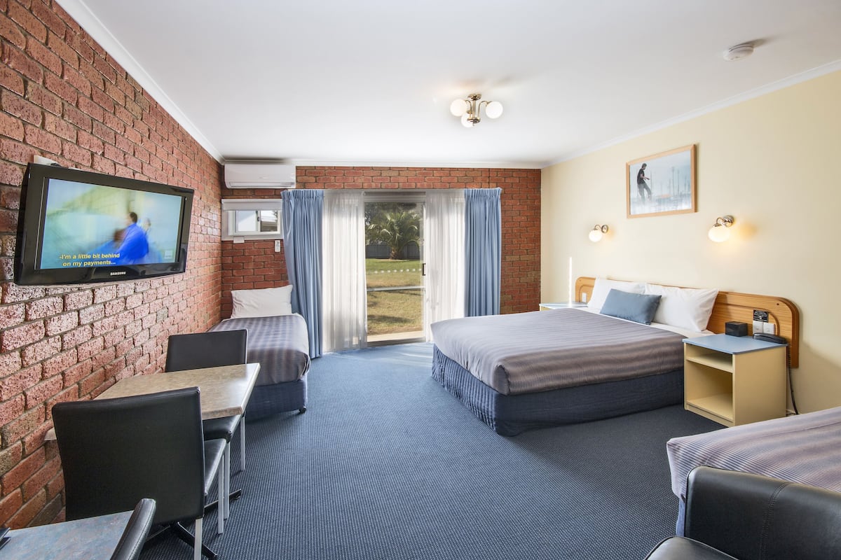 A hotel room with a brick wall, a television, a bed, a desk, and a view of the outdoors.