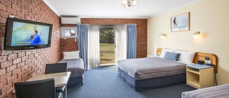 A hotel room with a brick wall, a television, a bed, a desk, and a view of the outdoors.
