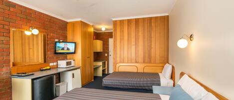 A compact hotel room with two beds, a small kitchenette, a television, and a brick wall.