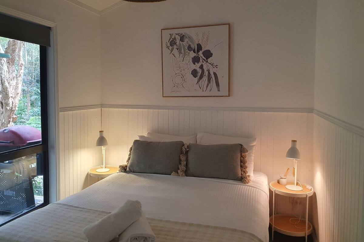 A neatly made bed with a white comforter and pillows, a framed artwork above it, and two bedside tables with lamps.