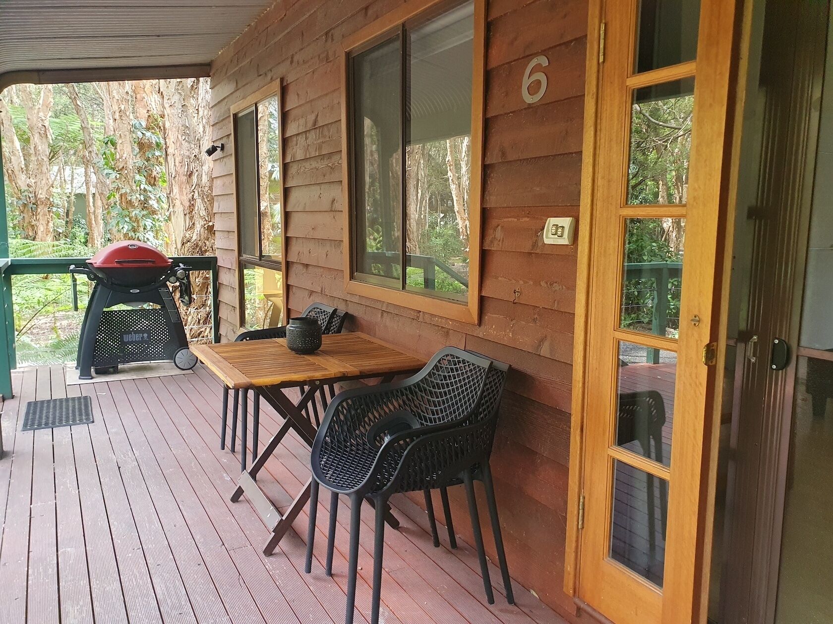 A wooden cabin with a covered porch, a grill, and a table with chairs.