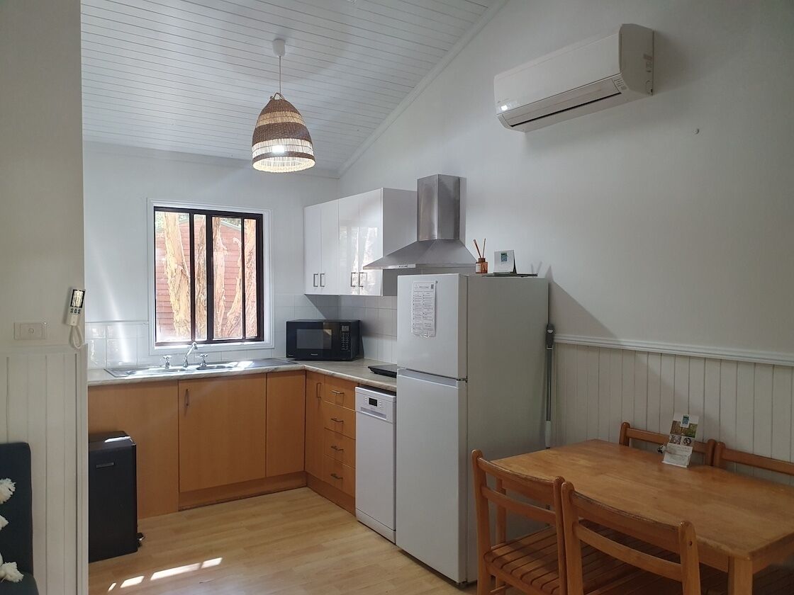 Una cocina compacta con armarios blancos, microondas, refrigerador y una mesa de comedor de madera.