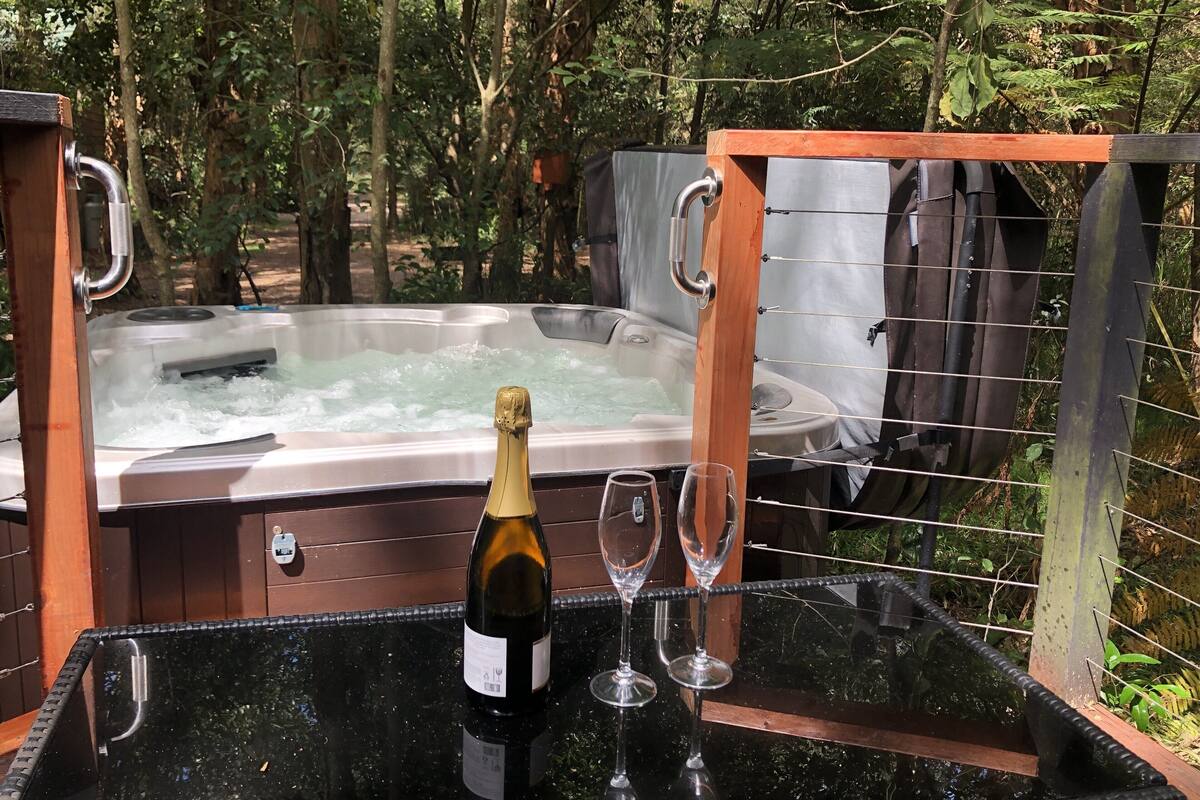 A hot tub with a wooden frame and metal handles, surrounded by a metal fence.