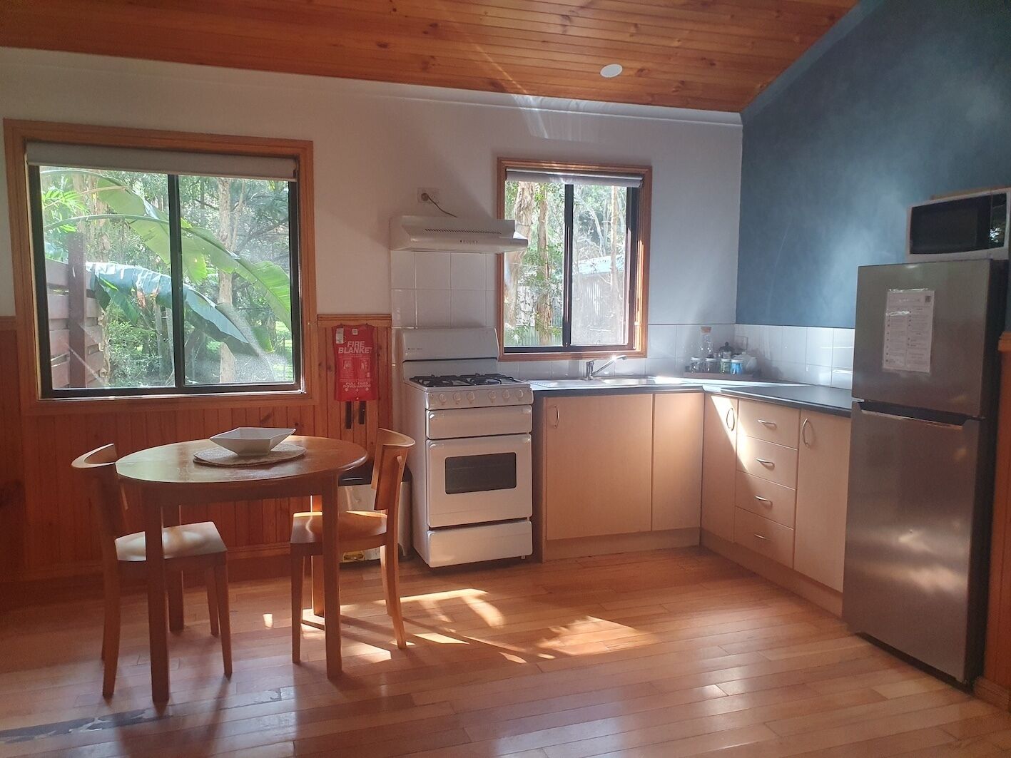 Cozinha compacta com armários de madeira, fogão a gás, geladeira e área de jantar com mesa e cadeiras.