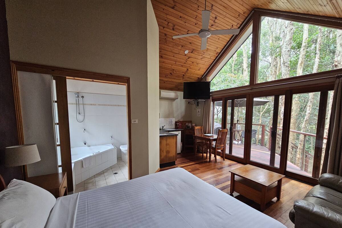 A bedroom with a large bed, a wooden ceiling fan, and a view of a balcony with a dining table and chairs.