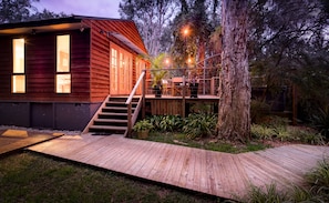 Una cabaña de madera con terraza, escaleras y zona de estar al aire libre, rodeada de árboles.