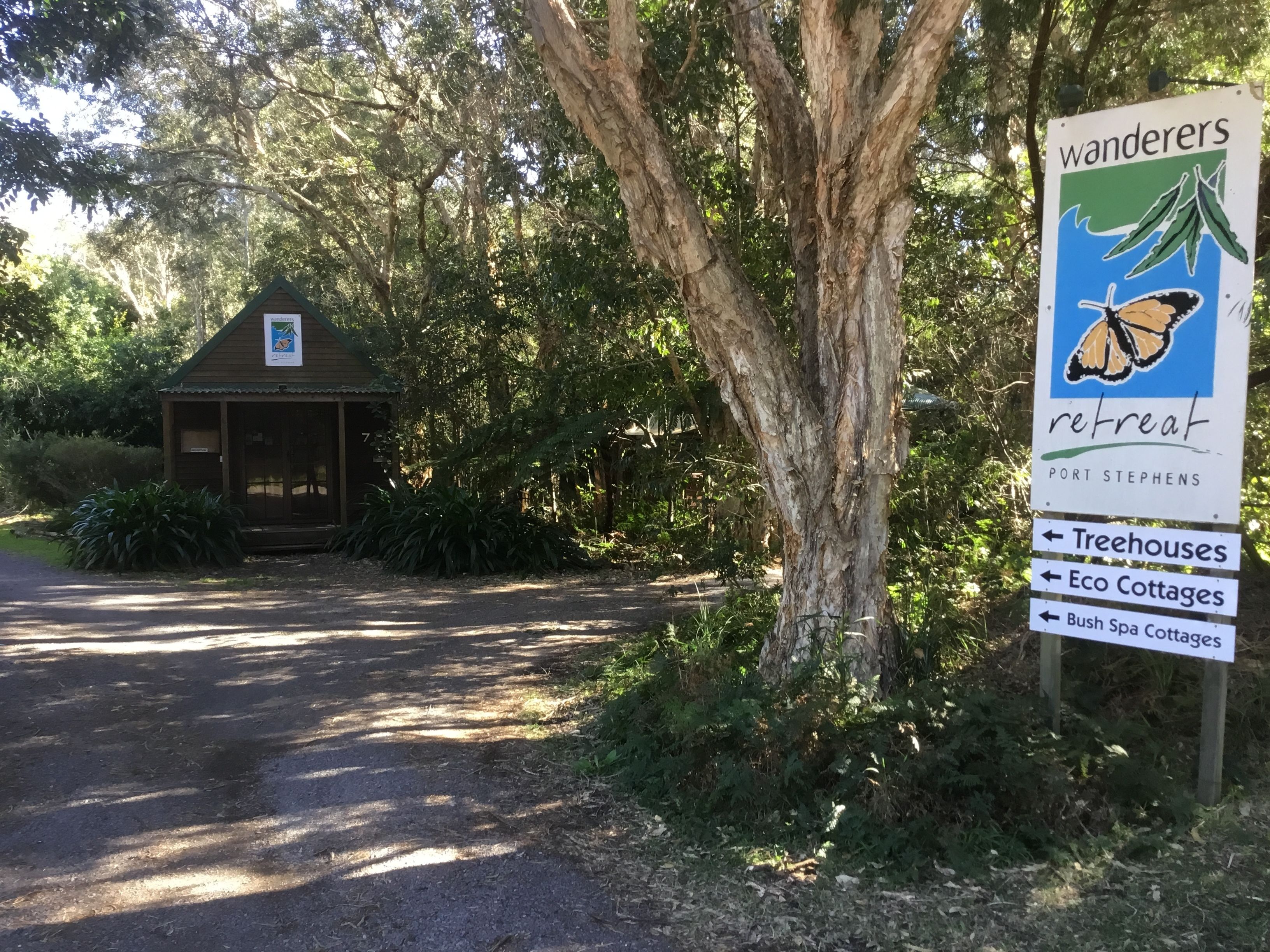 Une pancarte indiquant le chemin vers un centre de retraite appelé « Wanderers », avec des indications pour les « cabanes dans les arbres », les « éco-gîtes » et les « gîtes avec spa en pleine nature ».