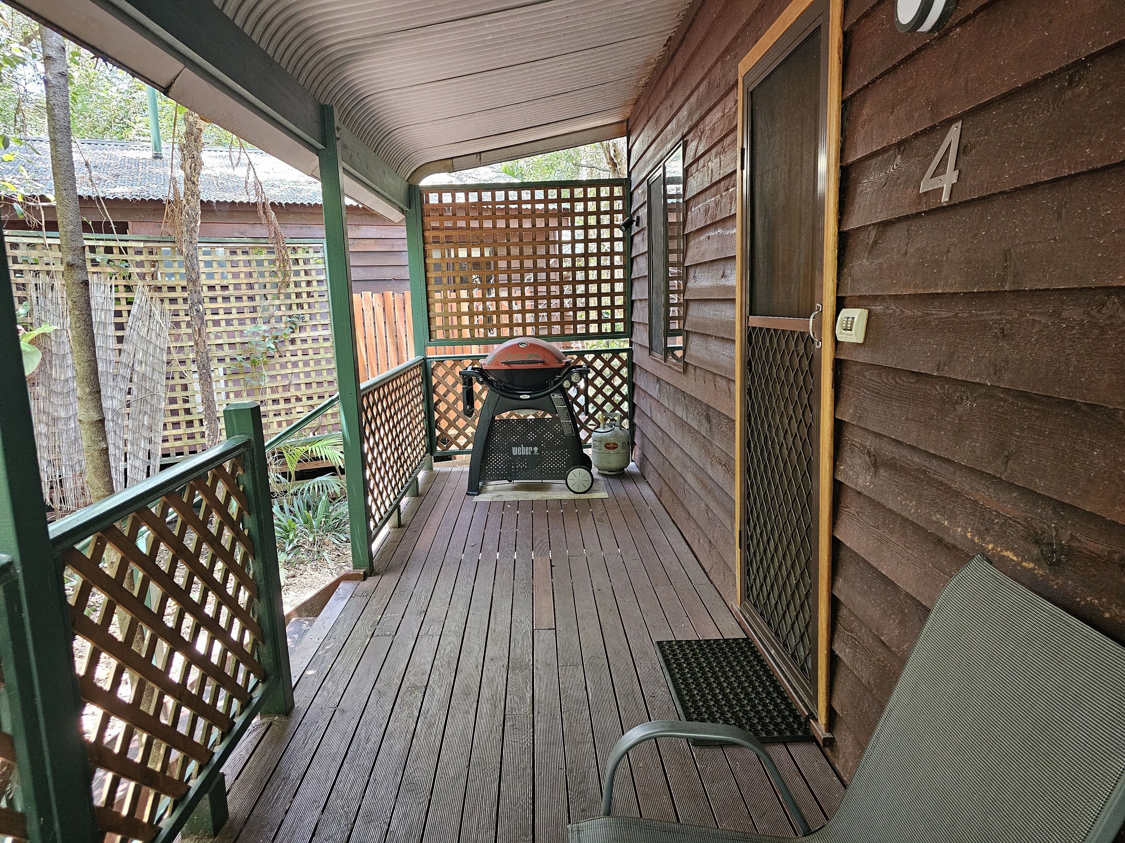 A covered porch with a grill, a chair, and a wooden fence.