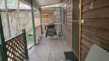 A covered porch with a grill, a chair, and a wooden fence.