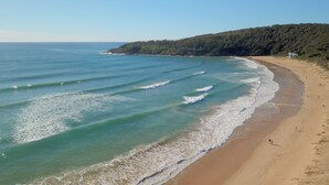 A beach with clear turquoise water, a sandy shore, and a forested hill in the background. - Wanderers Retreat Port Stephens (Boat Harbour)