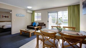 A hotel room with a bed, a sofa, a dining table with chairs, a small coffee table, and a window with curtains. - Beachpark Apartments (Coffs Harbour)