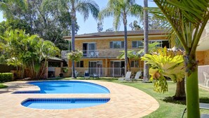 A two-story building with a swimming pool, surrounded by palm trees and a well-maintained lawn. - Beachpark Apartments (Coffs Harbour)