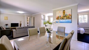 A modern living room with a dining area, a kitchen, and a bedroom. - Beachpark Apartments (Coffs Harbour)