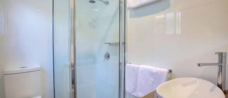 A modern bathroom with a glass-enclosed shower, a white toilet, and a sink with a towel hanging on the wall.
