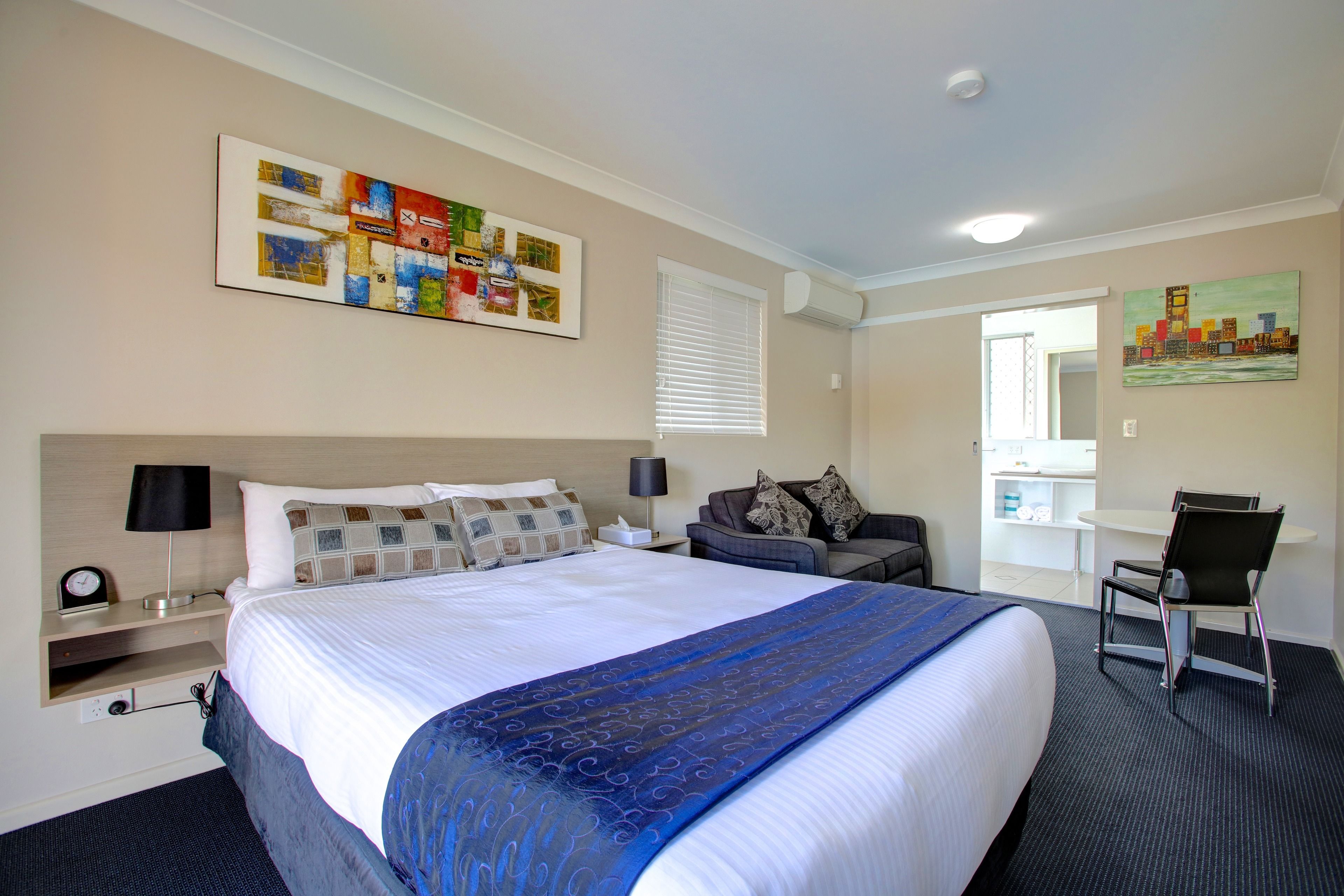 A hotel room with a large bed, a desk, a chair, and artwork on the walls.