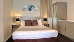 A hotel room with a large bed, two bedside tables with lamps, a wardrobe, and a painting on the wall. - Beachpark Apartments (Coffs Harbour)