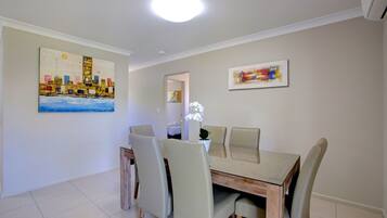 A dining area with a wooden table and four chairs, two paintings on the walls, and a ceiling light.