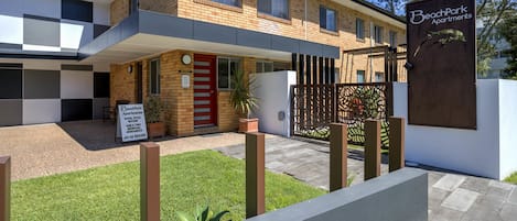 A modern two-story apartment building with a red door, a signboard, and a gated entrance.
