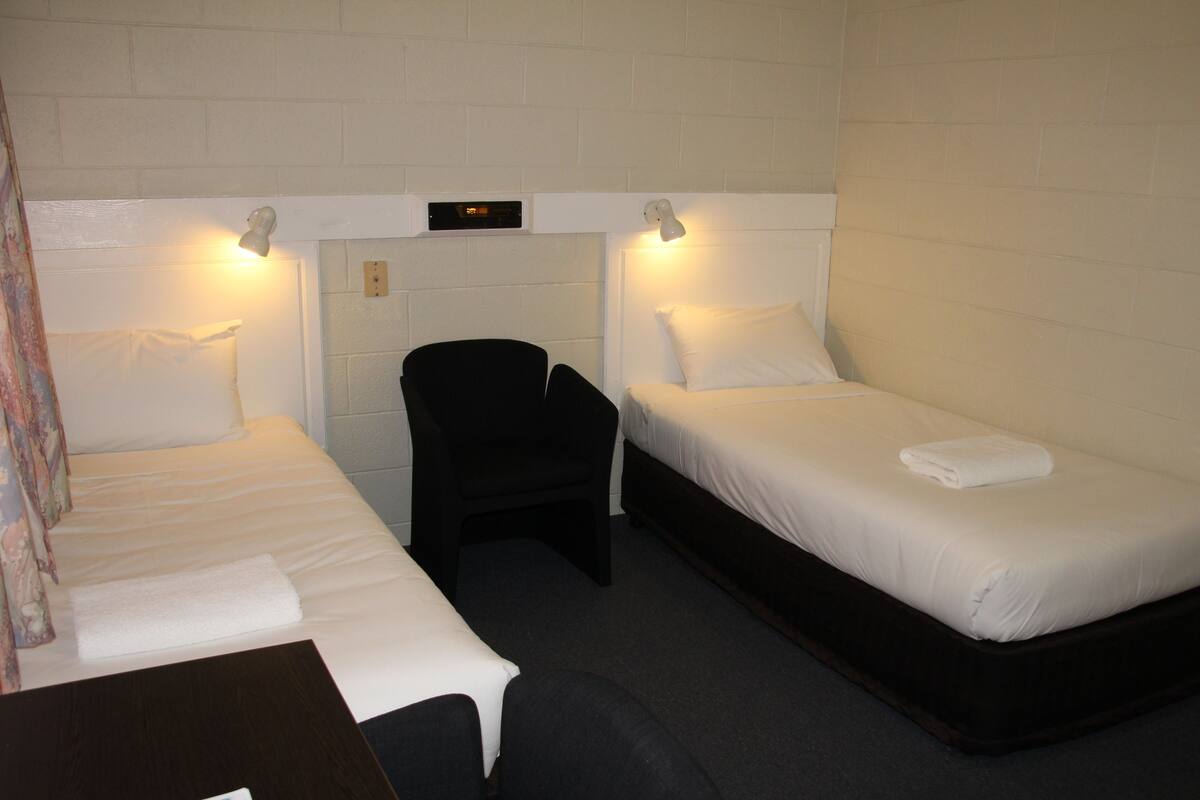 A small, clean room with two single beds, a chair, and a desk.