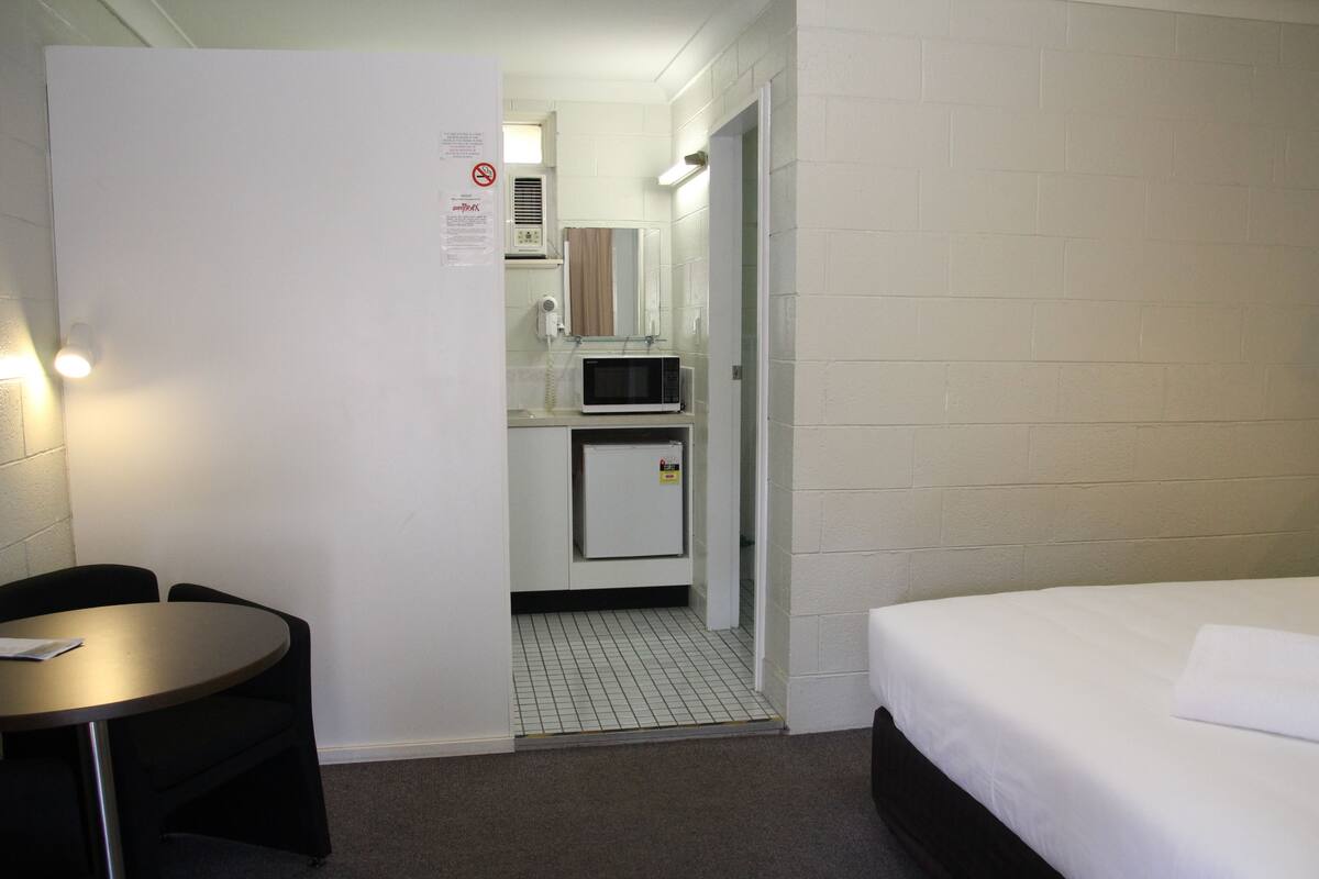 A hotel room with a bed, a small kitchenette, a microwave, and a table with a chair.