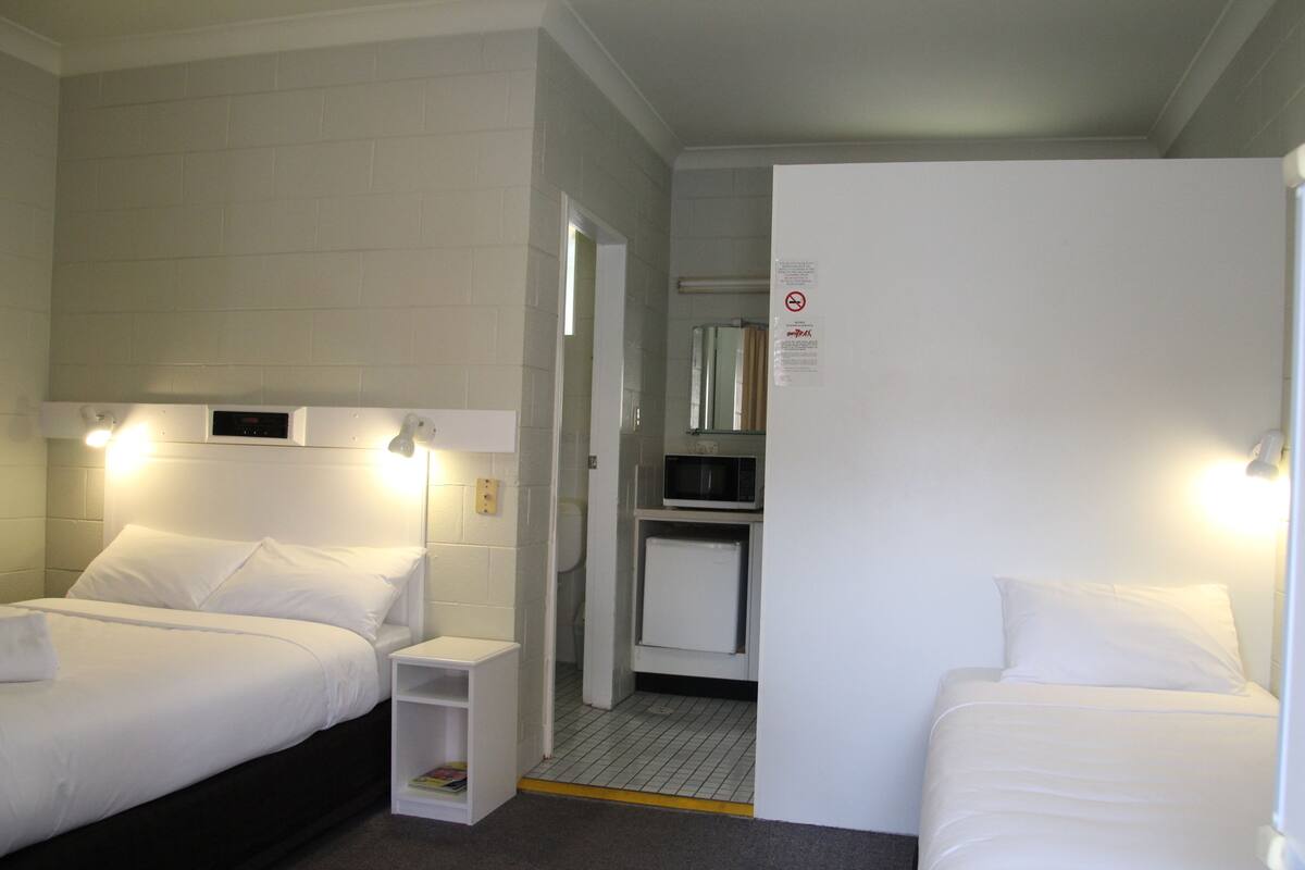 A hotel room with two beds, a small kitchenette, and a door leading to a bathroom.