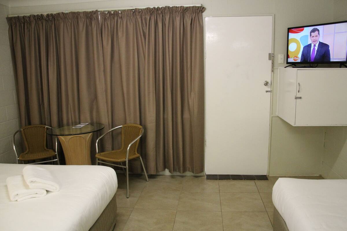 A hotel room with two beds, a television, a small table with chairs, and a curtain.