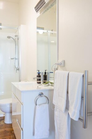 A modern bathroom with a white sink, a glass shower enclosure, a toilet, and a towel rack with two towels. - Highbury Apartments (East Launceston)