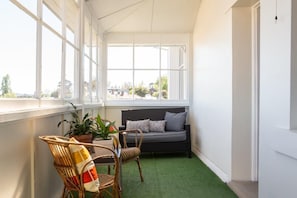 A room with a green artificial turf floor, a grey sofa with patterned cushions, wicker chairs, and potted plants. - Highbury Apartments (East Launceston)