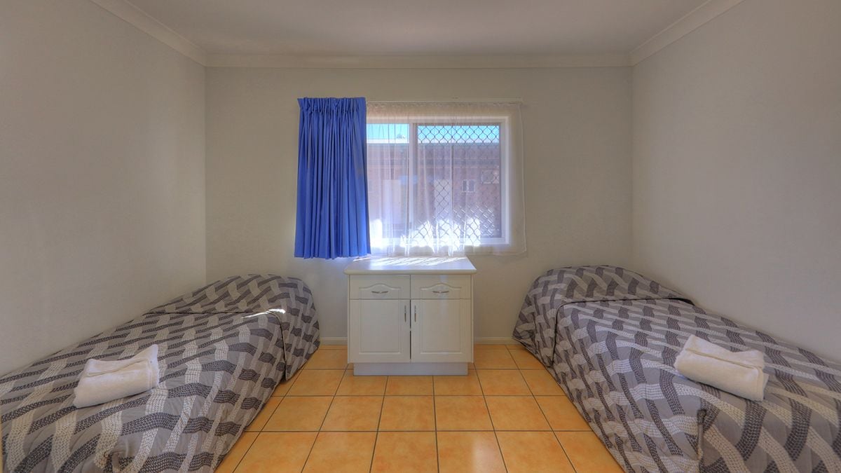 A small room with two beds, a window with a blue curtain, and a white cabinet.