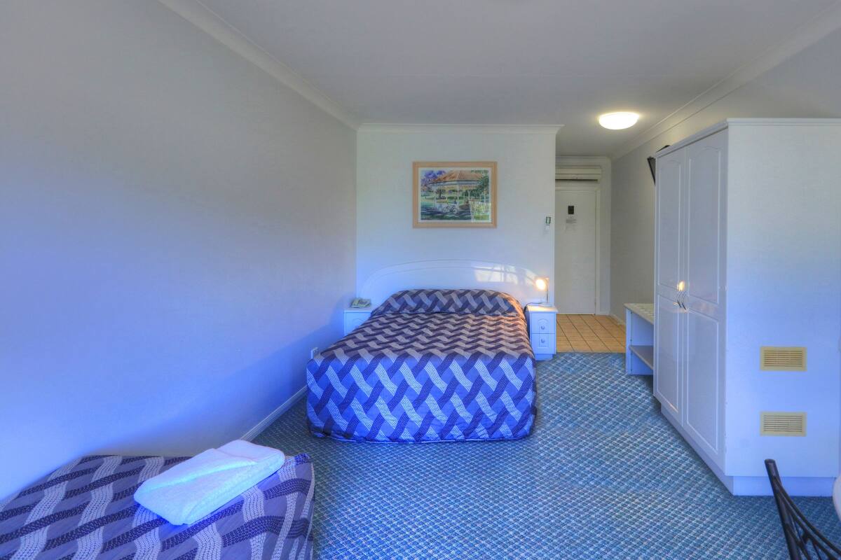 Una habitación pequeña y ordenada con una cama, una mesita de noche, una silla y un armario.