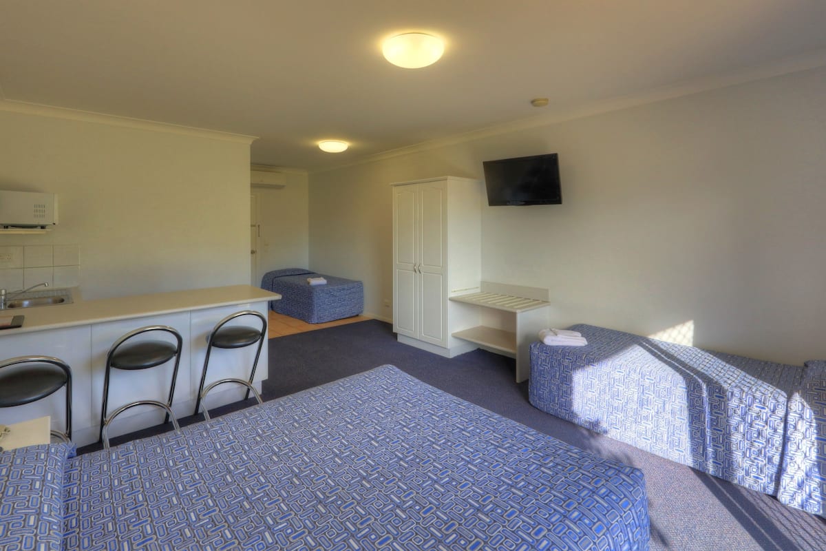 Habitación de hotel con dos camas, una kitchenette pequeña, un televisor y un armario.