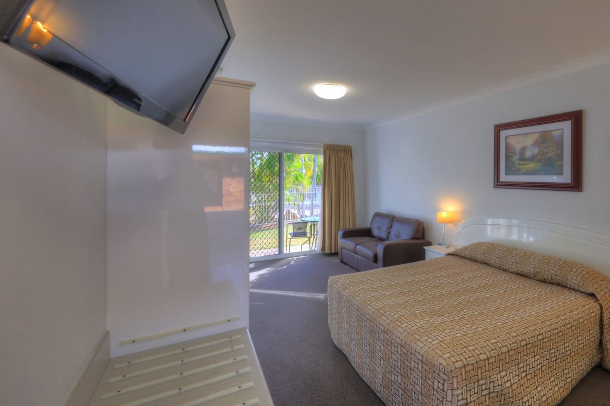 Una habitación de hotel con cama, sofá, televisor, un cuadro y ventana con cortinas.