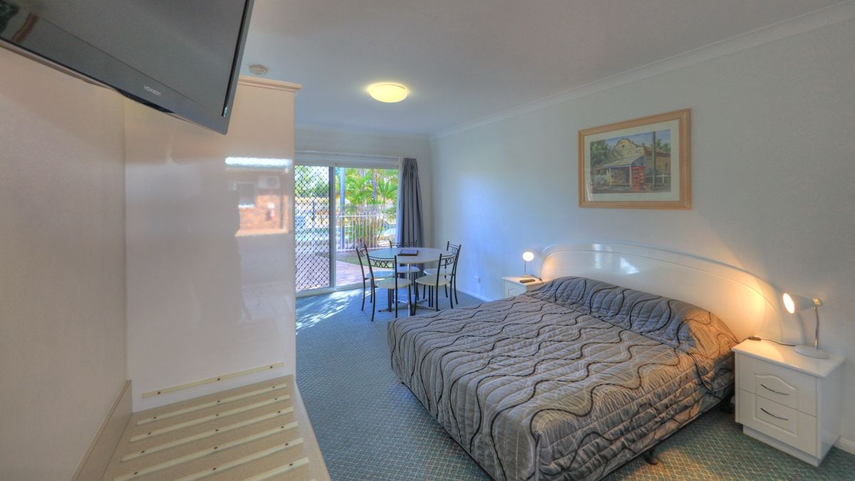 A bedroom with a bed, bedside table, and a window overlooking a patio area with a table and chairs.