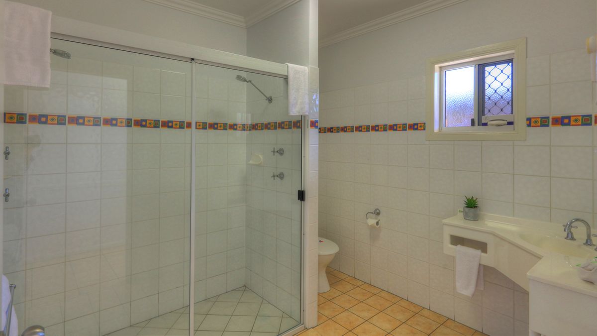 A bathroom with a glass-enclosed shower, a toilet, a sink, and a window.