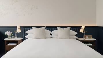 Una cama bien hecha con un cabecero oscuro, dos mesitas de noche con lámparas, y una pared con un diseño de hojas.