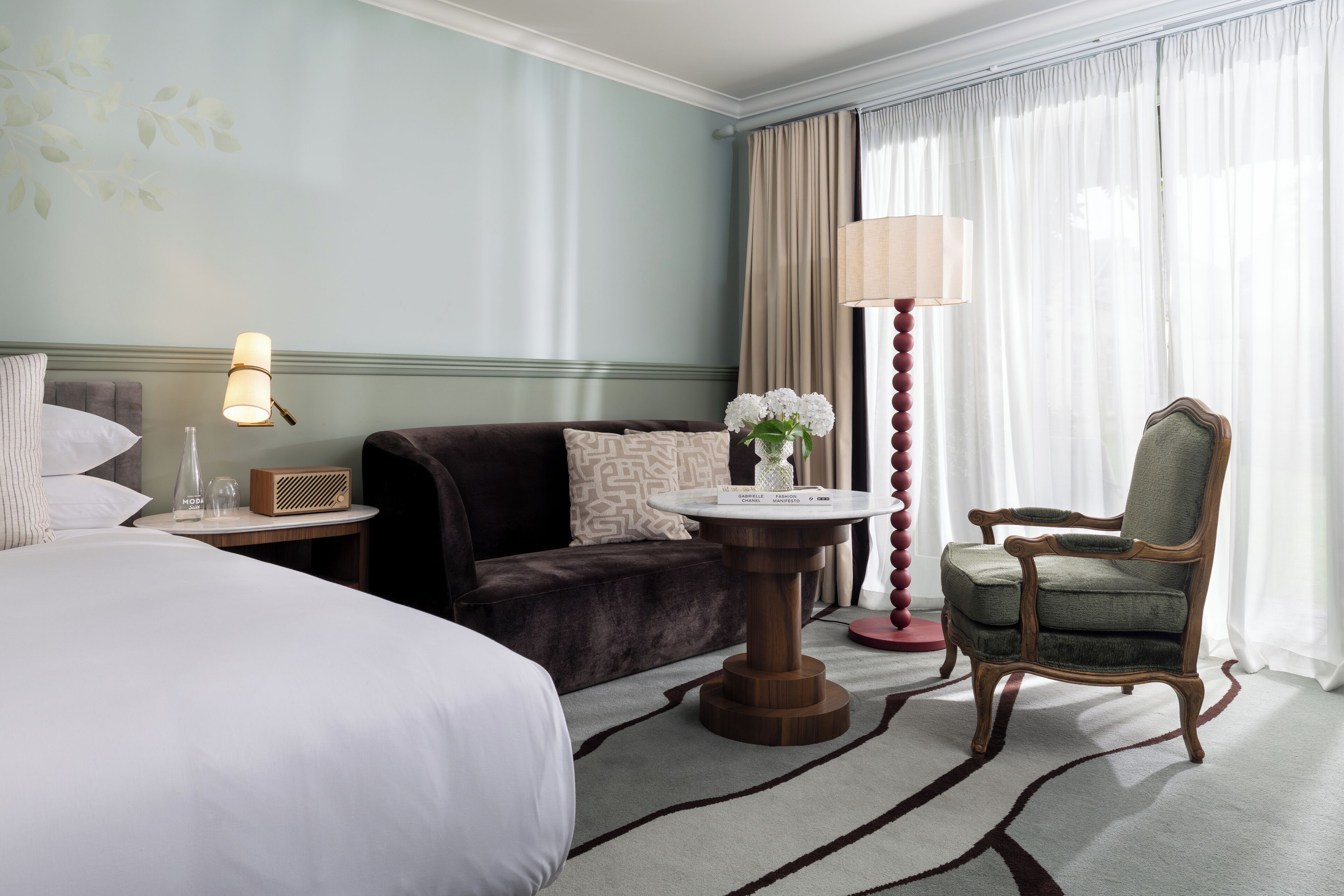 Una habitación de hotel con cama, sofá, sillón, mesita y lámpara.
