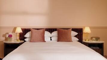 A hotel room with a large bed, two bedside tables, a nightstand, a lamp, a vase with flowers, and a radio.
