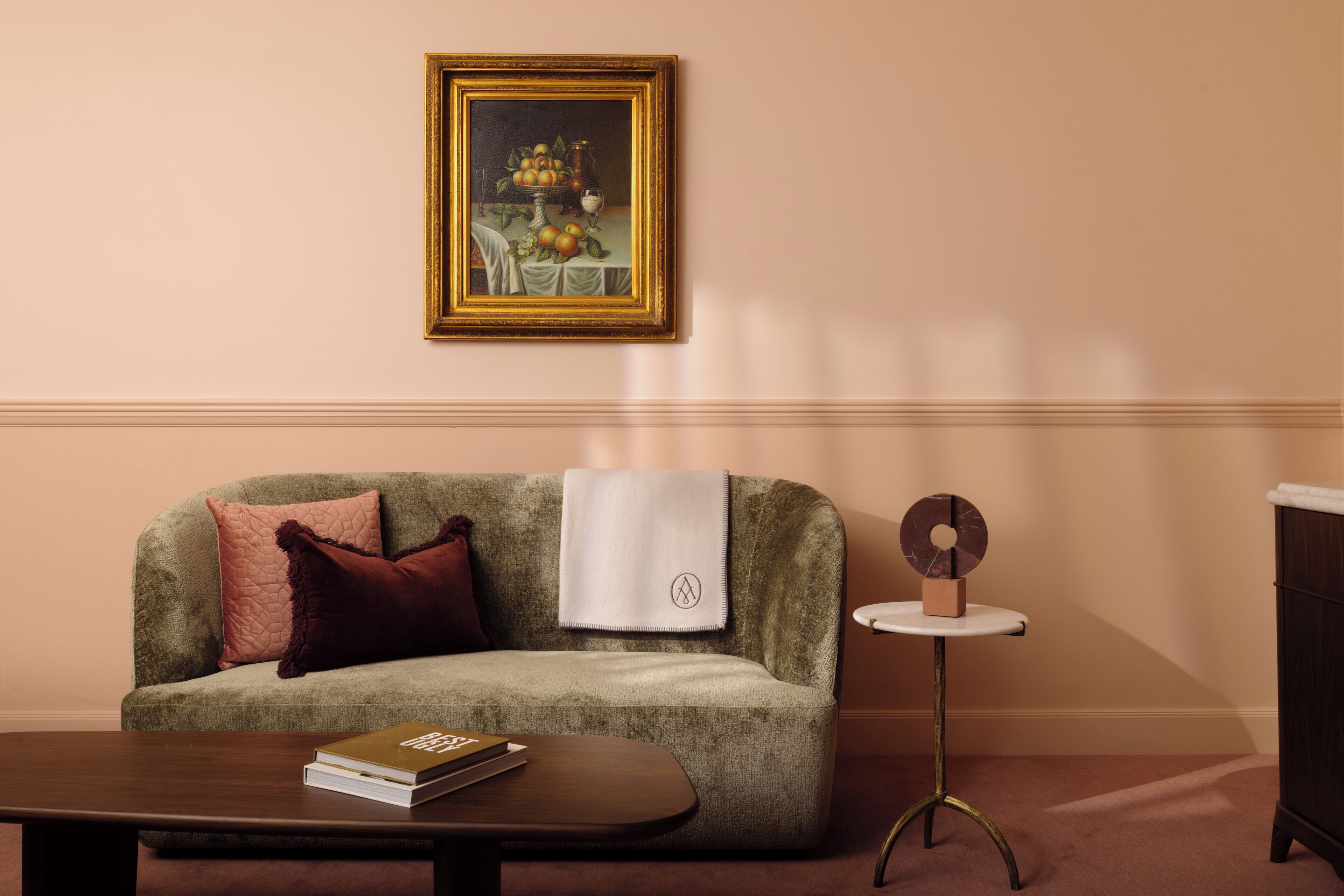 Uma sala de estar com um sofá verde, uma mesa redonda pequena, um quadro emoldurado e um livro sobre uma mesa de centro.