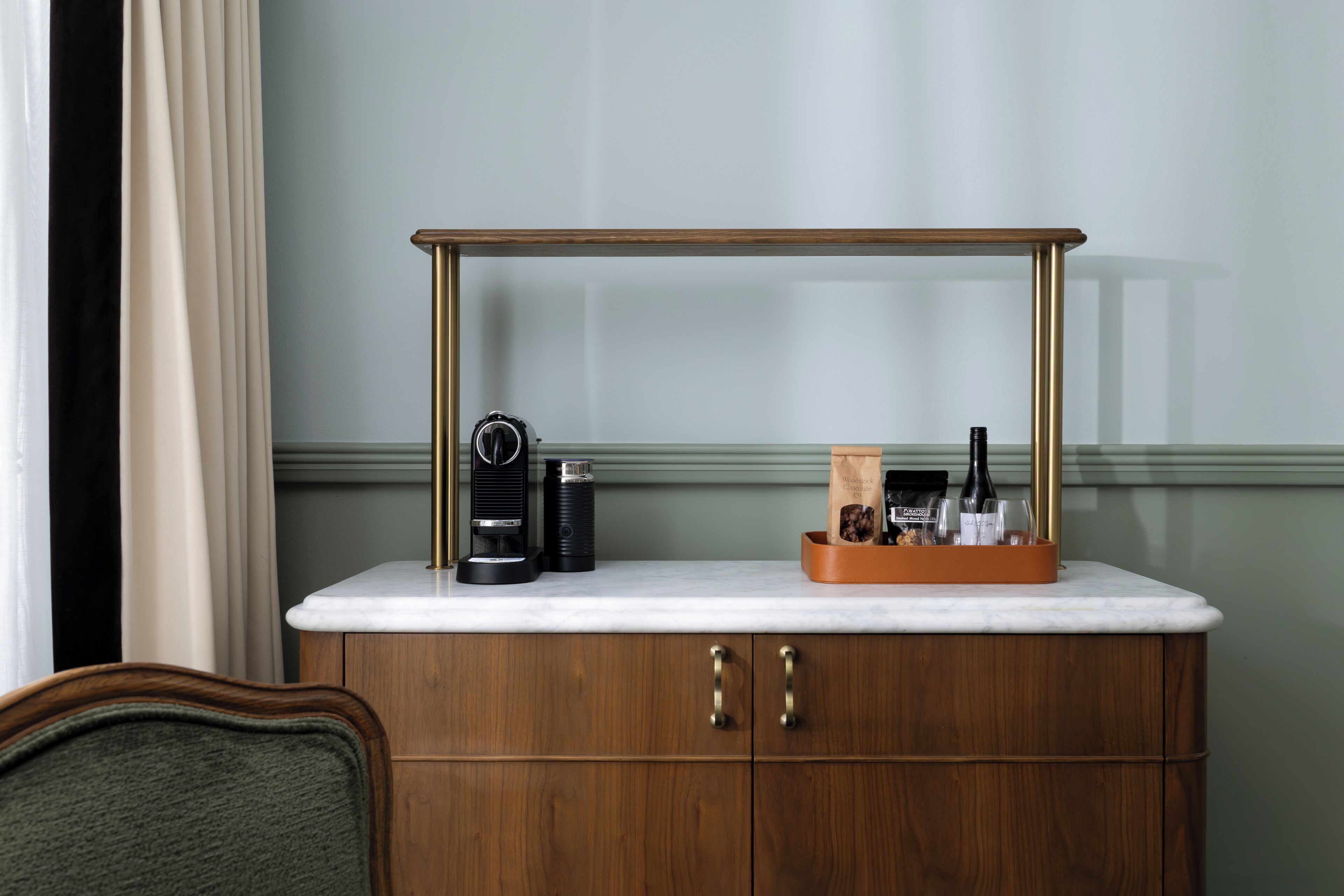 A wooden cabinet with a marble countertop, a coffee maker, and a tray with bottles and glasses.