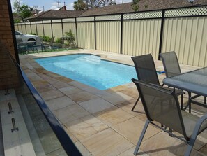 Ein Garten mit Schwimmbad, Terrassenmöbeln und einem umzäunten Bereich.
