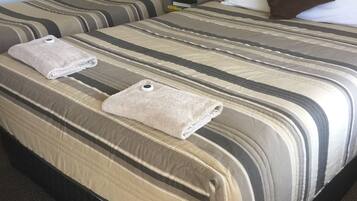 A hotel room with two beds, each with striped bedding and pillows. There are two bedside tables with lamps.