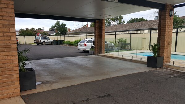 A covered parking area with a swimming pool, brick pillars, and a clear view of the street.
