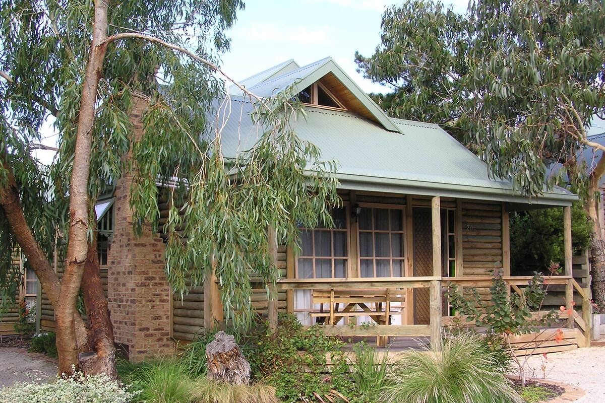 A rustic log cabin with a porch, surrounded by native vegetation.