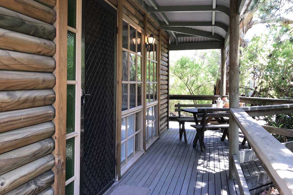 A wooden cabin with a covered porch, large windows, and a picnic table.