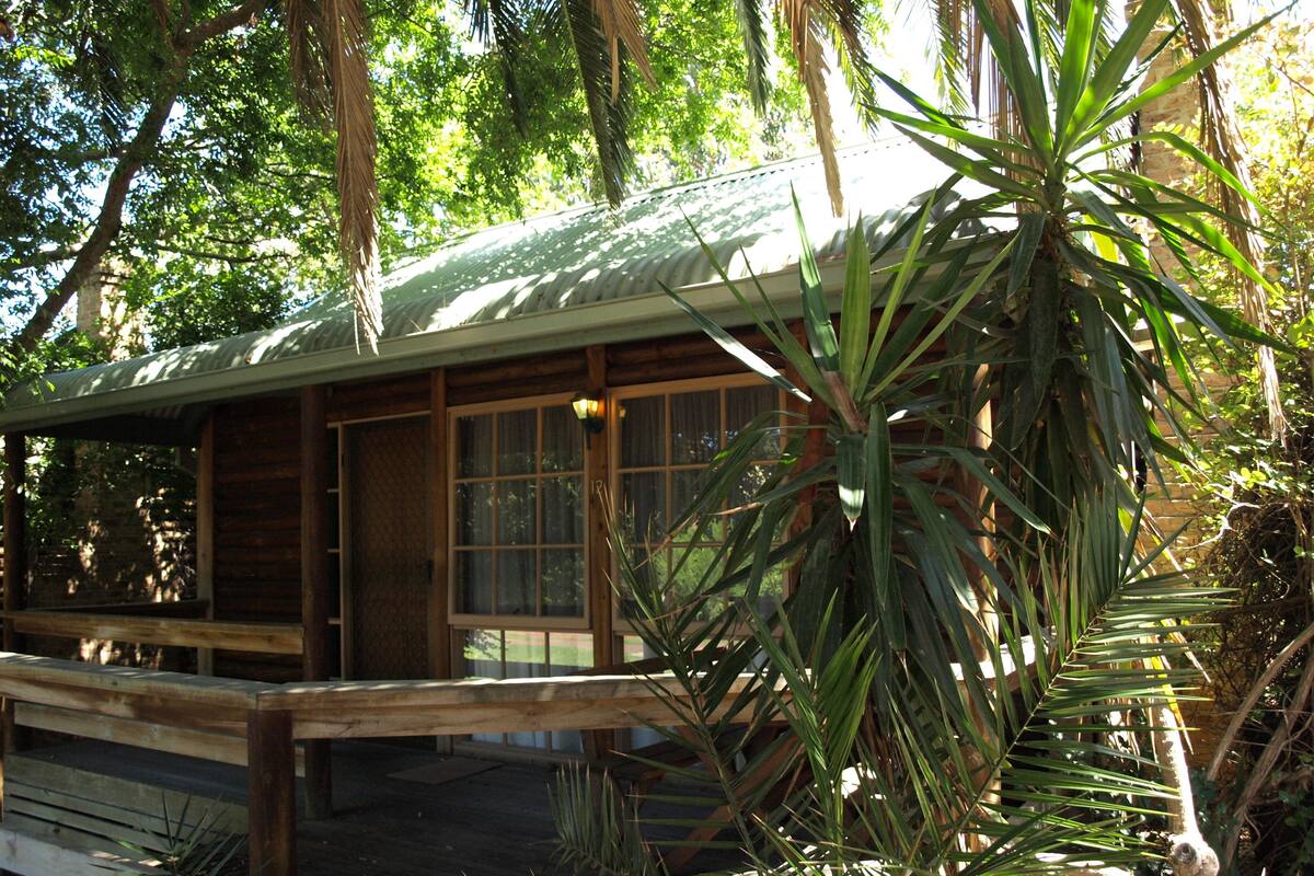 A wooden cabin with a sloped roof, large windows, and a wooden deck.
